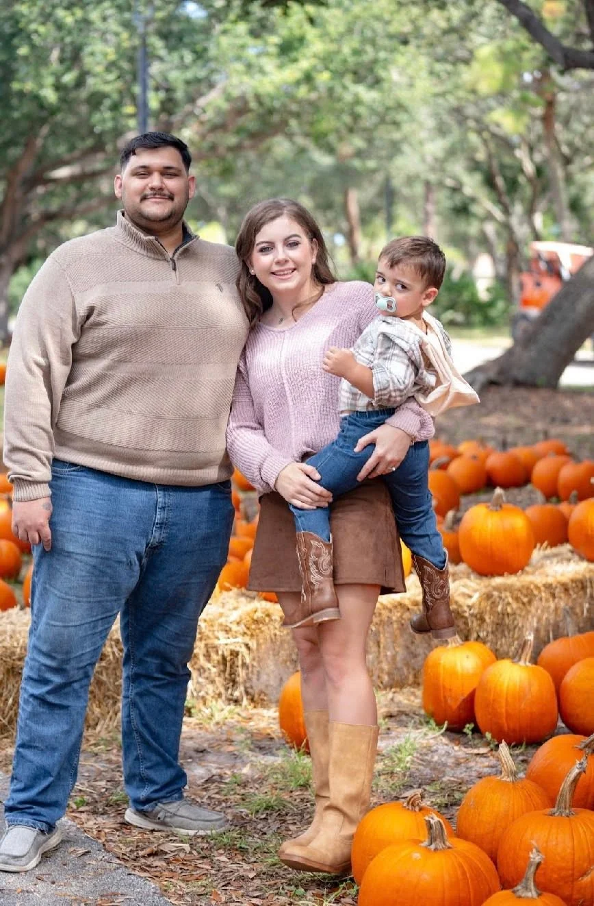Two adults and a child among pumpkins and hay bales