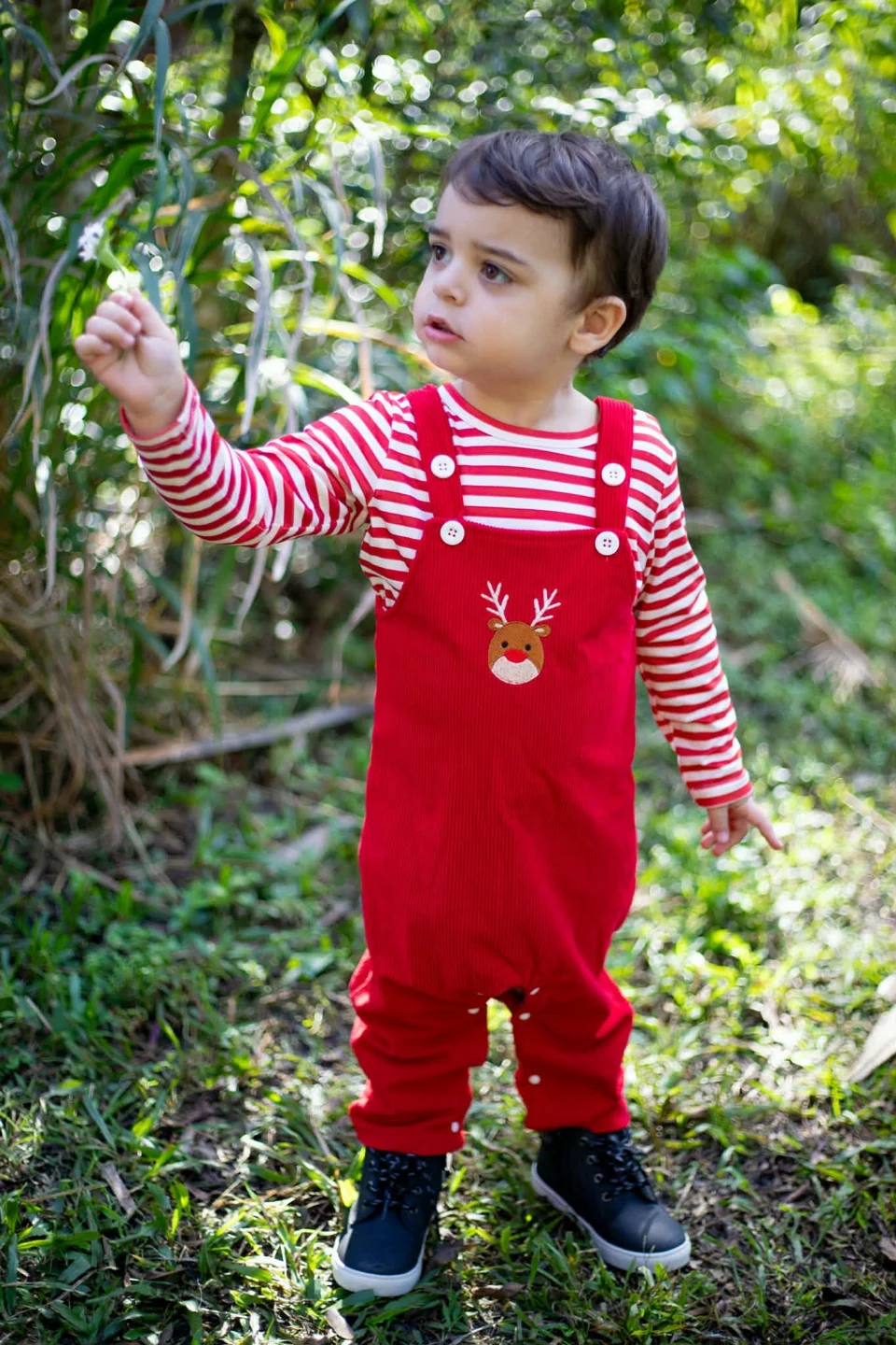 A young child outdoors wearing red reindeer overalls